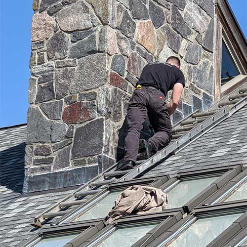 Chimney Repairs-Tech climbing up the side of a stone chimney on roof.
