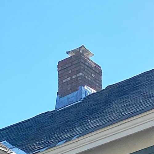 Masonry Repair-Black shingle roof with metal flashing around bottom of Chimney-Rutland Chimney