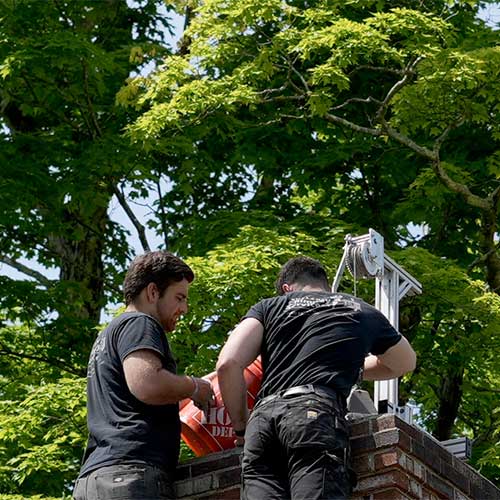 Two techs pouring ceramic coating down chimney with trees in the background and a winch on top of chimney-Rutland Chimney